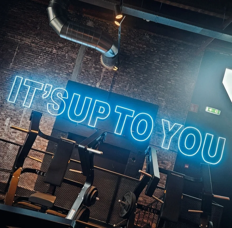 Blauwe neonletters It's up to you op een bakstenen muur boven krachttoestellen