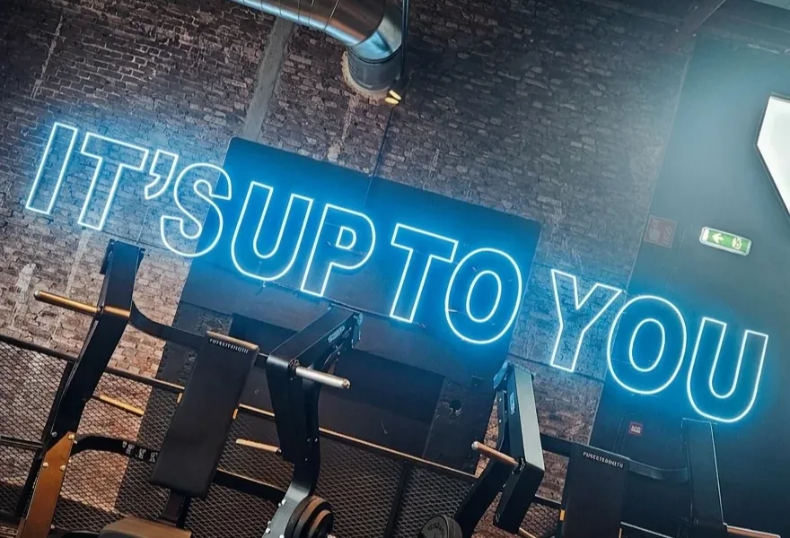Blauwe neonletters It's up to you op een bakstenen muur boven krachttoestellen