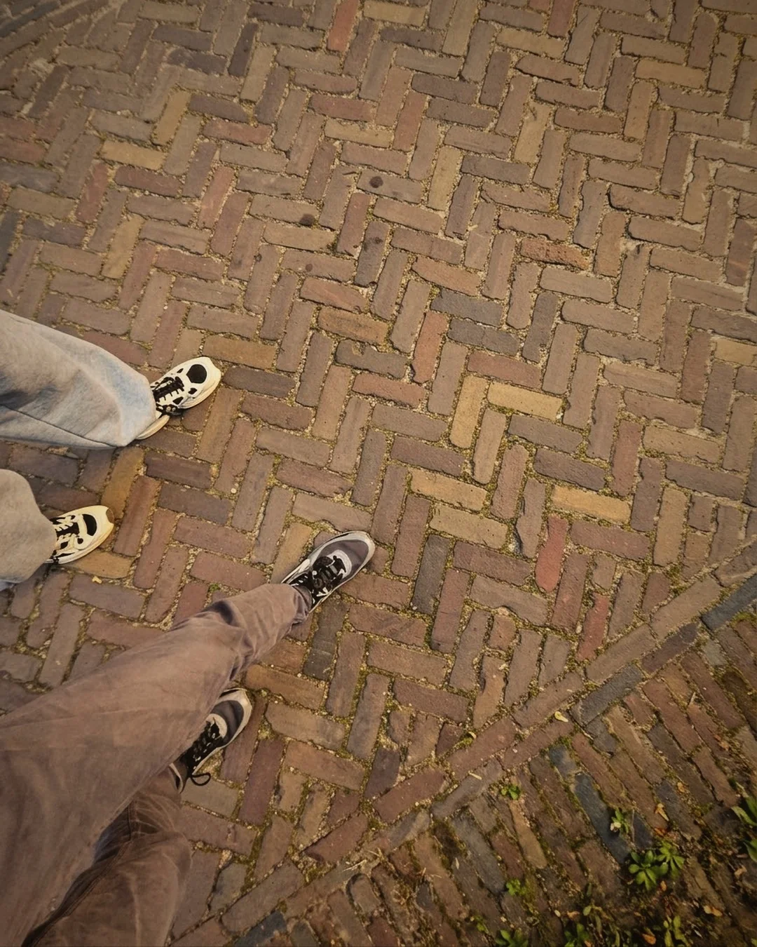 Wandelen voor je gezondheid: twee paar voeten in sneakers op een klinkerstraat, van bovenaf gezien